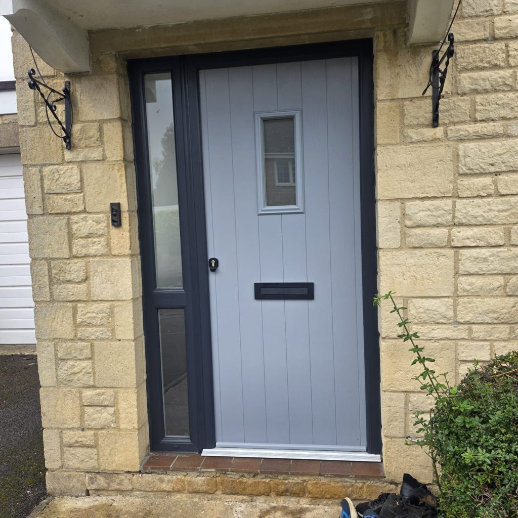 Grey composite front door with a glazed side panel, fitted in a Cotswold stone porch