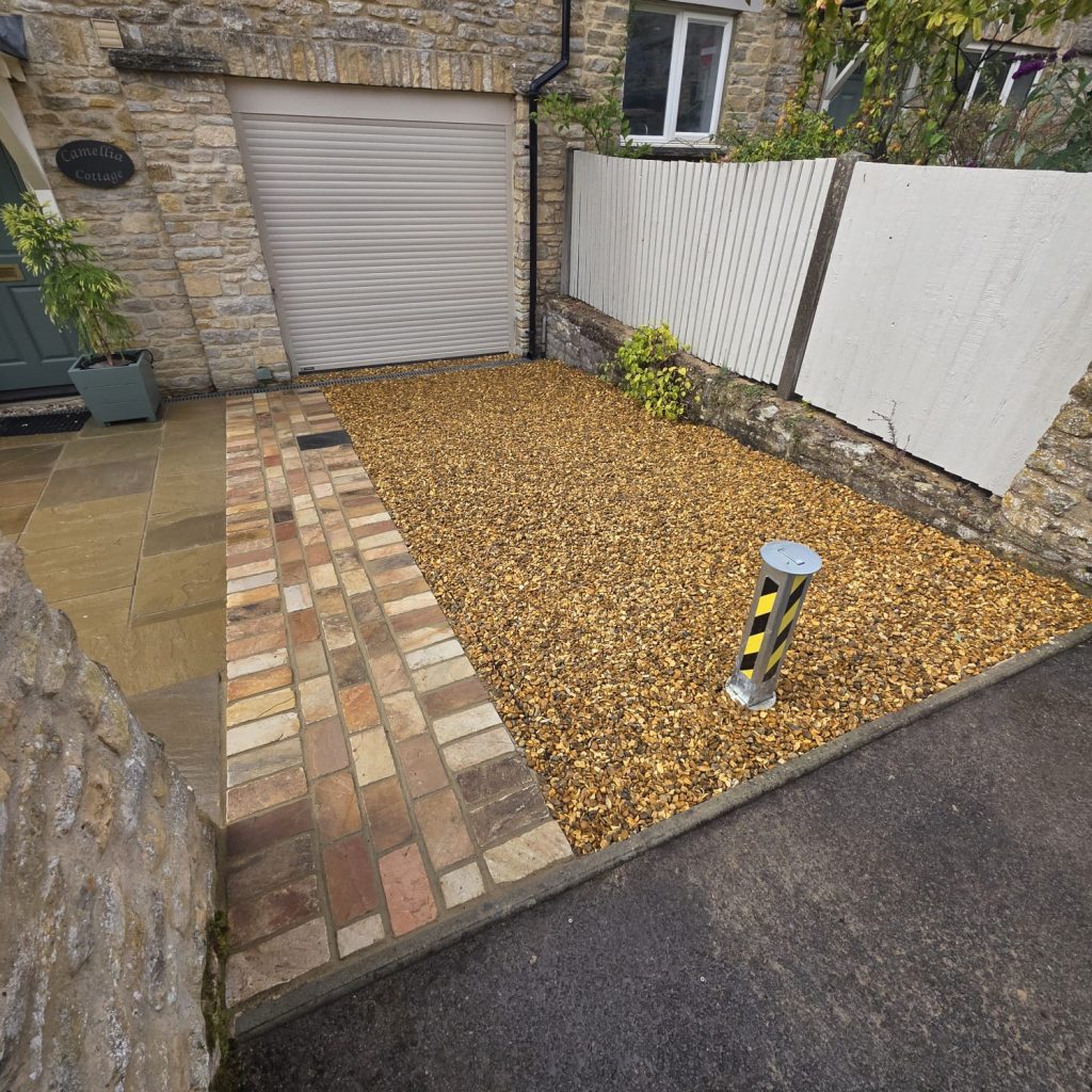 New gravel driveway with a block-paved path in front of a stone house and garage