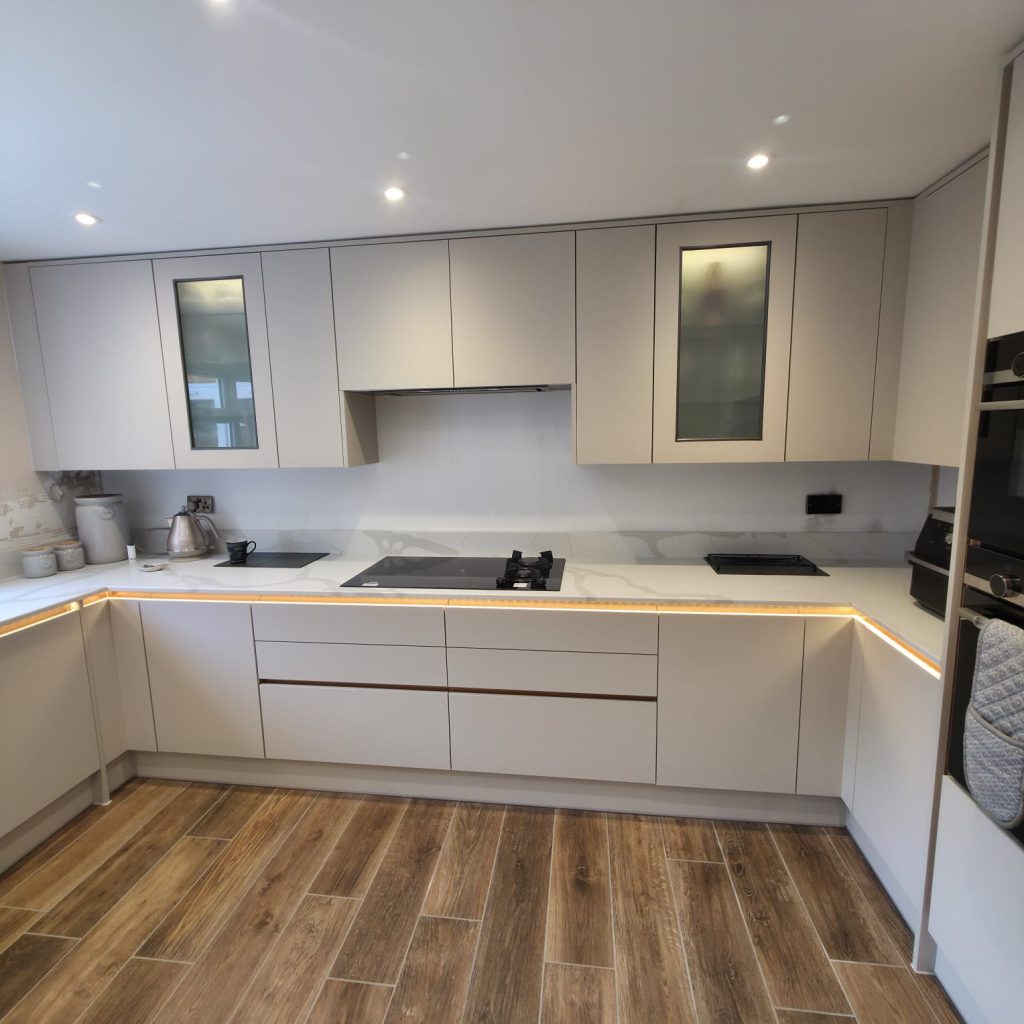 Kitchen with light grey handleless units, glazed wall cabinets, under-cabinet lighting and wood-effect flooring